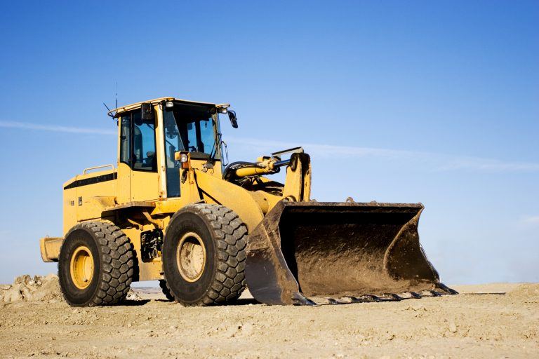 Yellow bulldozer parked on a dirt construction site under a clear blue sky.